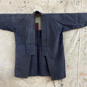 May include: A dark blue and white striped cotton kimono with a green and purple lining. The kimono is open in the front and has long sleeves.
