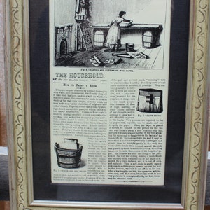 May include: A framed black and white illustration of a woman using a ladder to hang a picture on a wall. The illustration is from a vintage magazine called "The Household" and includes text about how to hang a picture.