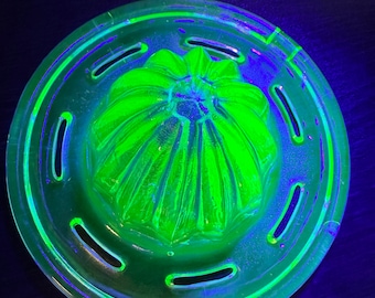 May include: A green glass citrus juicer with a fluted design and a base with six holes. The juicer is illuminated with a black light, causing it to glow.