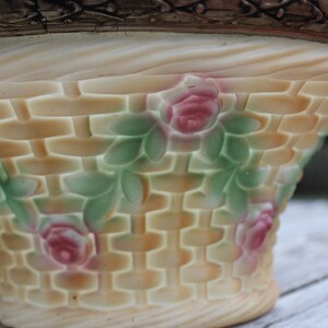 May include: A ceramic planter shaped like a basket with a woven pattern and floral details. The planter is decorated with pink roses and green leaves.