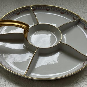 May include: A white divided serving platter with a gold handle and trim. The platter has a central bowl and five sections. The rim features a decorative pattern with blue, red, and gold accents.