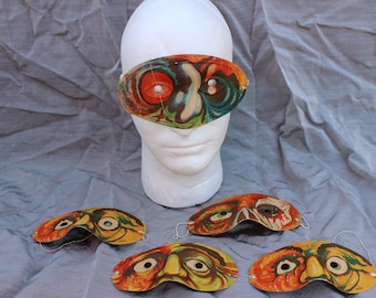 May include: Five colorful paper Halloween masks with a monster design. The masks have large eyes and a green, orange, and red color scheme. The masks are on a gray surface.