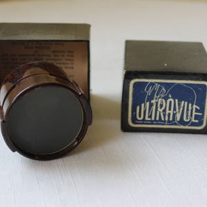 May include: A vintage Ultravue brand magnifying glass in a brown plastic case with a black lens. The case is closed and the magnifying glass is visible through the opening.