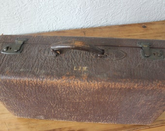 May include: Vintage brown leather suitcase with a handle and metal clasps. The suitcase has a textured surface and the initials "L.J.M." are embossed on the front. The suitcase is likely from the mid-20th century.