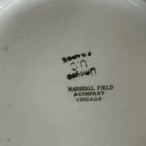 May include: Close-up of a white ceramic dish with black text. The text includes "U.C. France", "own", and "Marshall Field & Company Chicago". The dish has a slightly textured surface.