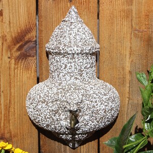May include: A white and brown ceramic water fountain with a spout, mounted on a wooden fence.