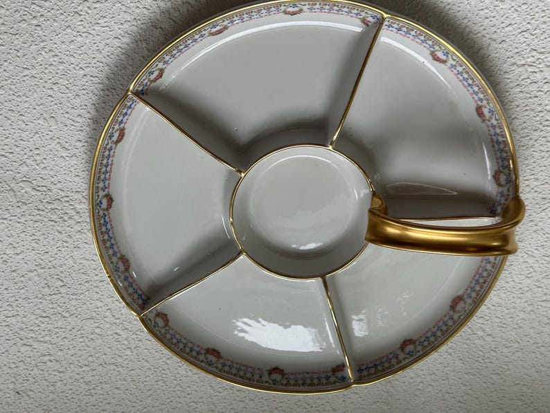 May include: A white divided serving platter with a gold handle and trim. The platter is divided into six sections, with a small round center section. The rim features a blue, red, and gold floral pattern.