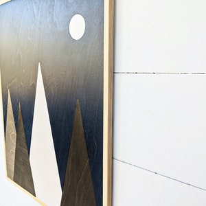 May include: A wooden wall art piece with a dark blue background and three white and brown triangles forming a mountain range. A white circle representing the moon is in the upper right corner.