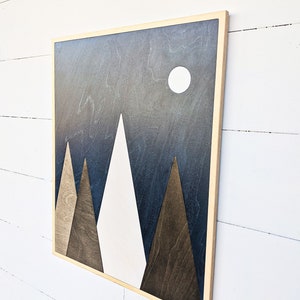 May include: A framed wood wall art piece with a geometric design of three triangles in shades of brown and white against a dark blue background with a white circle in the upper right corner.