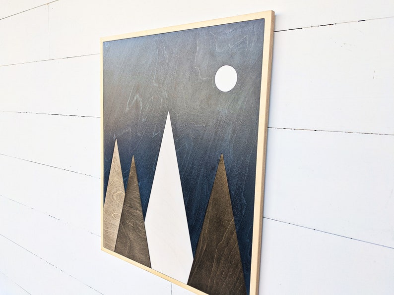 May include: A framed wood wall art piece with a geometric design of three triangles in shades of brown and white against a dark blue background with a white circle in the upper right corner.