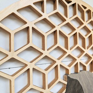 May include: A large, circular wooden wall decor with a geometric pattern of overlapping, hexagonal shapes. The wood is a light brown color and the pattern creates a 3D effect.