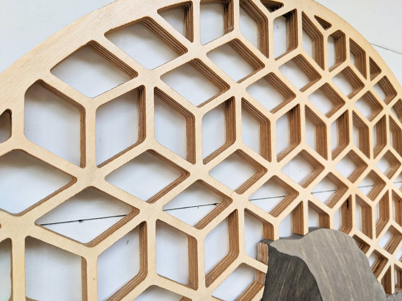 May include: A large, circular wooden wall decor with a geometric pattern of overlapping, hexagonal shapes. The wood is a light brown color and the pattern creates a 3D effect.