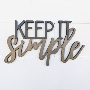 May include: Wooden sign with the text "Keep it simple" in black and brown lettering.