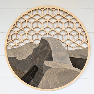 May include: A circular wooden wall art piece with a geometric pattern of hexagons. The center of the piece features a stylized mountain range in shades of brown and gray.