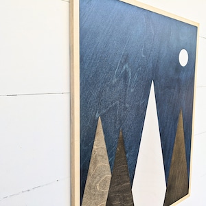 May include: A wooden wall art piece with a blue background and three white and brown mountains. A white circle representing the moon is in the upper right corner.