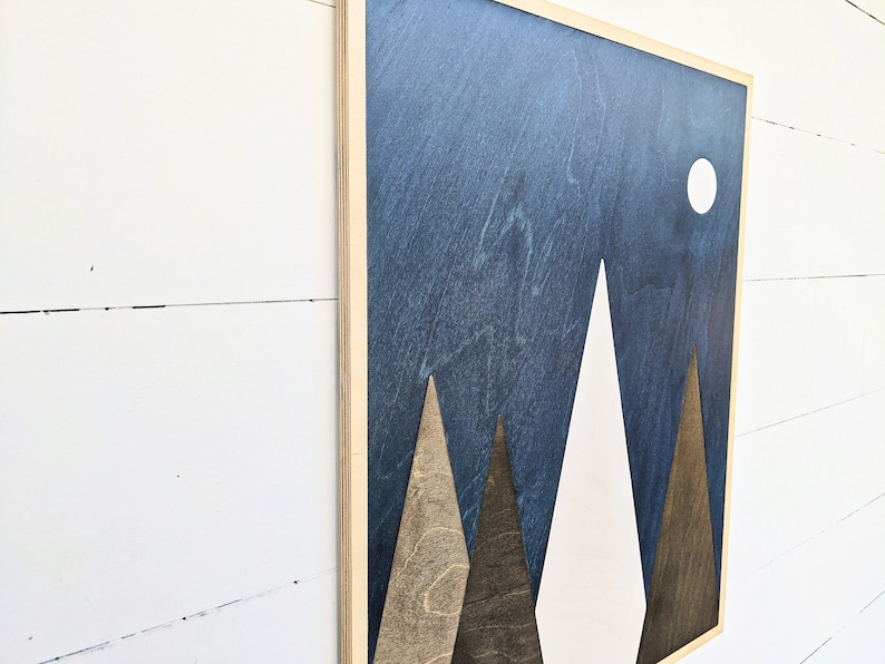 May include: A wooden wall art piece with a blue background and three white and brown mountains. A white circle representing the moon is in the upper right corner.