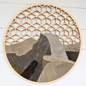 May include: A circular wooden wall art piece featuring a geometric pattern and a stylized depiction of Half Dome, a famous rock formation in Yosemite National Park.