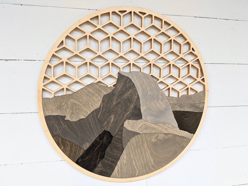 May include: A circular wooden wall art piece featuring a geometric pattern and a stylized depiction of Half Dome, a famous rock formation in Yosemite National Park.