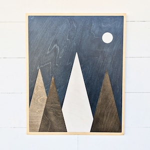 May include: A wooden wall art piece depicting a mountain range with a white moon in a dark blue sky. The mountains are made of different shades of brown wood.