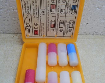 May include: A bright yellow plastic medical kit case containing various small cylindrical containers with colored caps. The interior lid features a printed instructional chart with Russian text and numbered diagrams for identifying the contents.
