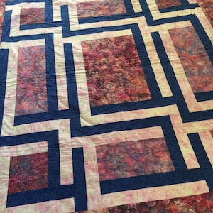 May include: A quilt with a geometric pattern of blue and white squares on a pink and purple background.