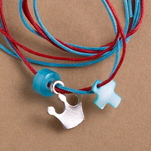 May include: A red and blue cord bracelet with a silver crown charm, a blue bead, and a light blue cross charm.