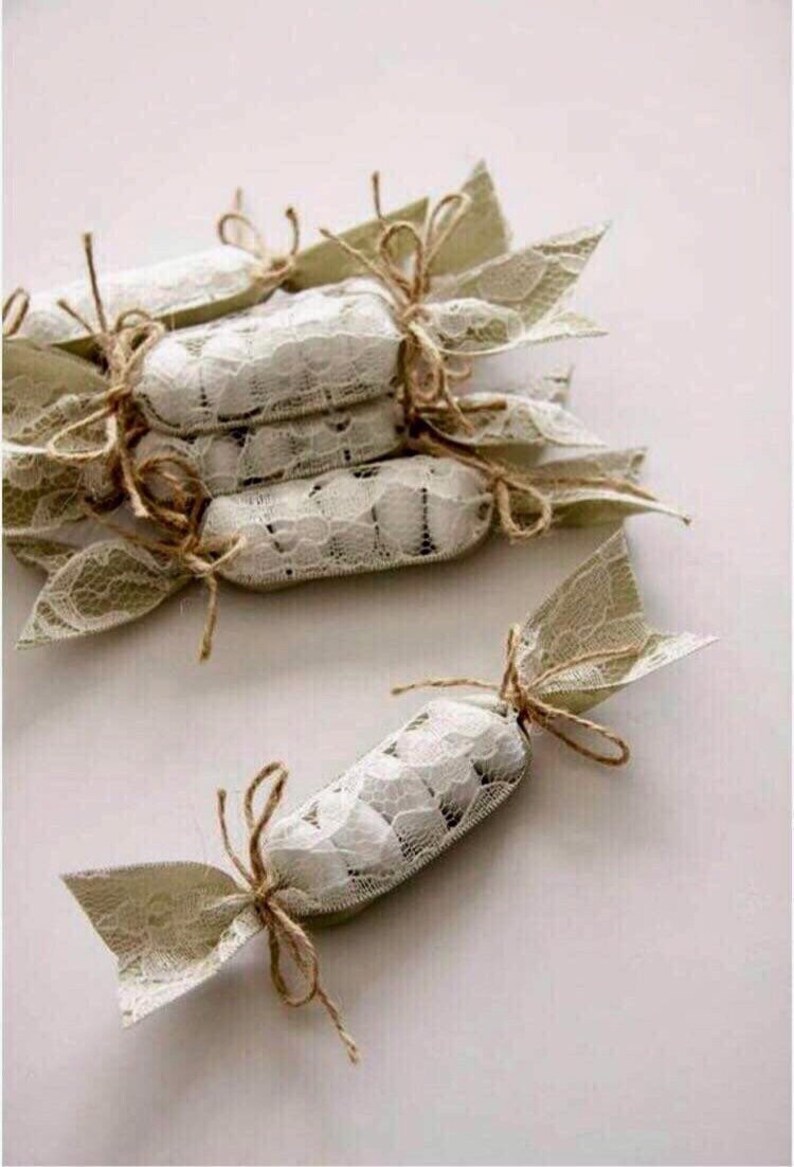 Puede incluir: Una pila de peque&ntilde;os favores blancos envueltos en encaje y atados con cuerda. Los favores tienen forma de caramelo y son perfectos para una boda u otra ocasi&oacute;n especial.
