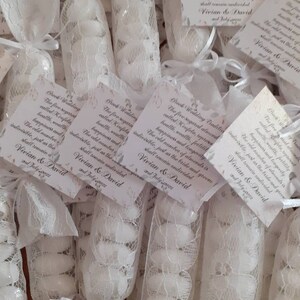 Puede incluir: Bolsitas de encaje blanco llenas de almendras blancas. Cada bolsa tiene una peque&ntilde;a tarjeta adjunta con el texto "Tradici&oacute;n griega de boda. Las cinco almendras azucaradas llamadas Koufeta, representan la salud, la riqueza, la fertilidad, la felicidad y la longevidad. El n&uacute;mero impar de almendras es indivisible, al igual que la novia y el novio permanecer&aacute;n indivisibles. Vivian & David 2 de julio de 2022."