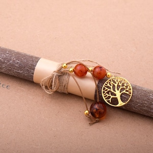 Può includere: Una candela di legno marrone con un ciondolo a forma di albero della vita dorato e perline ambrate. La candela è avvolta da uno spago e ha un'etichetta bianca con il testo "my tree".