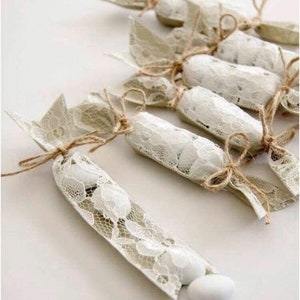 Puede incluir: Una fila de peque&ntilde;as bolsas de regalo de encaje blanco atadas con cordel y llenas de caramelos blancos.
