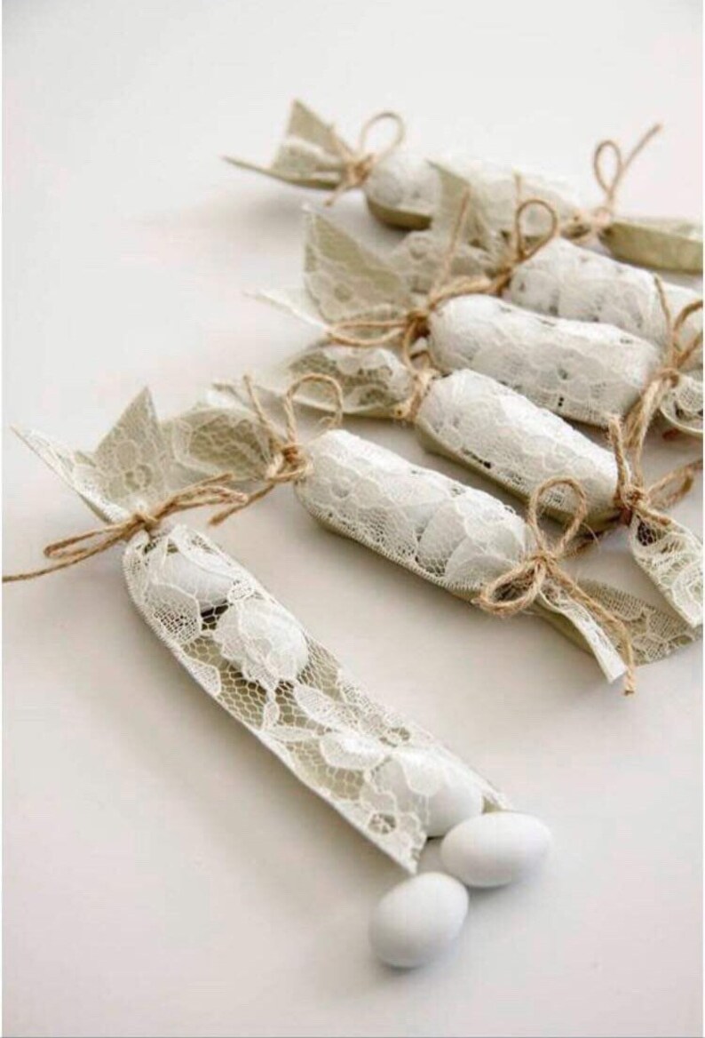 Puede incluir: Una fila de peque&ntilde;as bolsas de regalo de encaje blanco atadas con cordel y llenas de caramelos blancos.