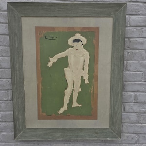 May include: A framed print featuring a figure in a white costume and hat against a green background, with the signature Picasso visible in the upper left corner. The artwork is enclosed in a wide, textured, light gray wooden frame with a mat.