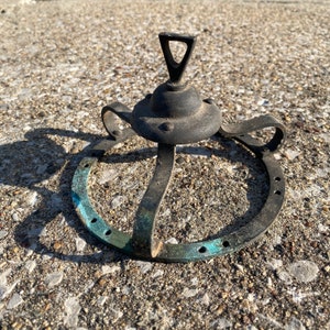 May include: A black metal crown with a circular base and a pointed top. The crown has a decorative design with a blue patina.