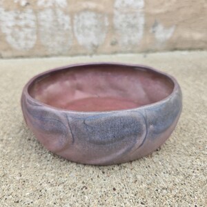 May include: A round ceramic bowl with a low profile and a wide opening. The exterior and interior feature a blended glaze of muted mauve, dusty rose, and soft slate blue tones, creating a smooth, swirling color transition across the surface.