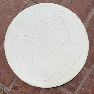 May include: White ceramic plate featuring a raised design of a woman holding a child. The design is minimalist, using simple lines.
