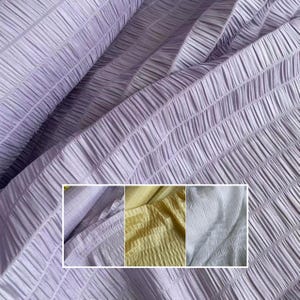 Può includere: Primo piano di un tessuto strutturato e plissettato in una morbida tonalità lavanda. Il tessuto è disposto in linee diagonali, creando un effetto increspato. Un inserto più piccolo mostra campioni di tessuti simili in giallo e azzurro.