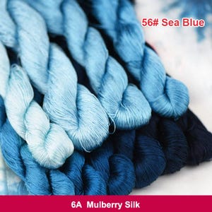 May include: Close-up of a bundle of blue and light blue silk embroidery floss. The floss is arranged in a layered, overlapping pattern. The text "56# Sea Blue" and "6A Mulberry Silk" is visible on the image.