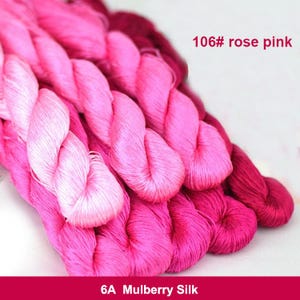 Puede incluir: Primer plano de un paquete de hilo de seda de morera rosa y blanco. El hilo está dispuesto en un degradado de blanco a rosa. La etiqueta dice "106# rose pink" y "6A Mulberry Silk".