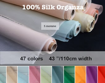 May include: Rolls of 100% silk organza fabric in various colors. The fabric is 43 inches wide and comes in 47 colors. The text "100% Silk Organza" and "5 momme" are visible on the fabric rolls.