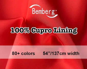 May include: Vibrant red fabric with the text "Bemberg" and "100% Cupro Lining." The image also states "80+ colors" and a width of "54"/137cm." The fabric appears to be smooth and flowing, with subtle texture.