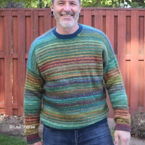 May include: A person wearing a green, blue, and orange striped sweater with a crew neck. The sweater has a fuzzy texture. The person is wearing blue jeans.