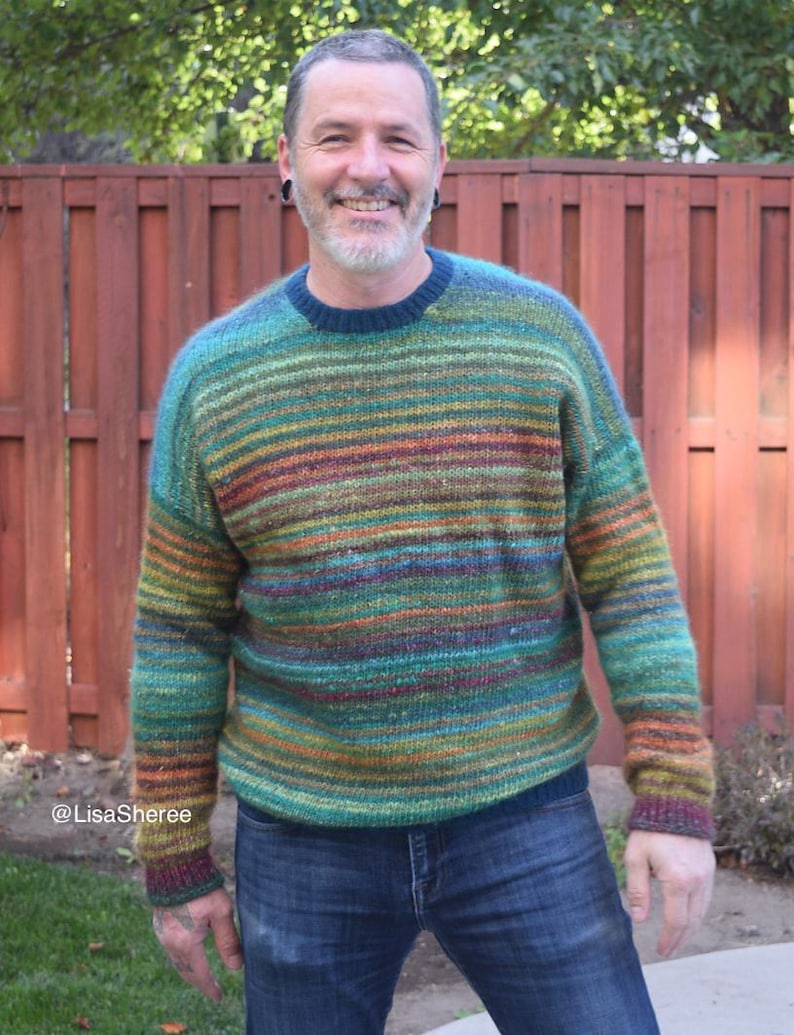 May include: A person wearing a green, blue, and orange striped sweater with a crew neck. The sweater has a fuzzy texture. The person is wearing blue jeans.