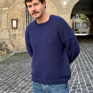 May include: A navy blue knitted sweater with a crew neck and long sleeves. The sweater is made of a soft, comfortable material and has a relaxed fit.
