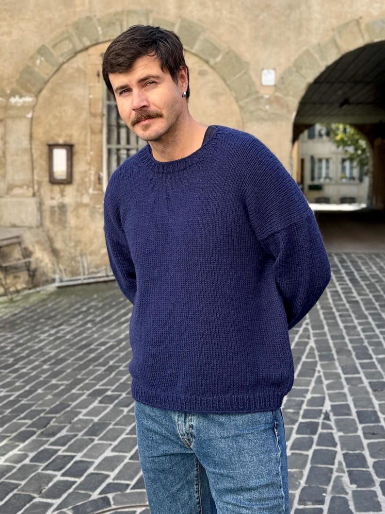 May include: A navy blue knitted sweater with a crew neck and long sleeves. The sweater is made of a soft, comfortable material and has a relaxed fit.