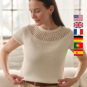 Op de afbeelding: Crèmekleurige gebreide top met een gedetailleerde open halslijn en korte mouwen. De top wordt gecombineerd met een beige broek en een bruine riem. De vrouw op de foto draagt gouden oorbellen.