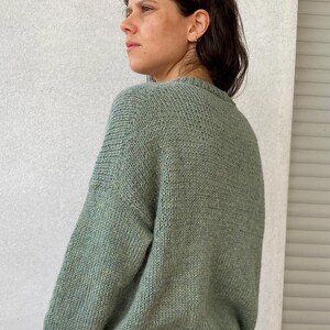 May include: A soft, green knitted sweater with a crew neck. The sweater is made with a textured stitch and has a relaxed fit.