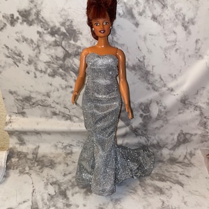 May include: A doll with brown hair styled in a bouffant wearing a silver sequined strapless gown.
