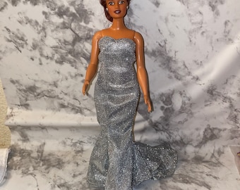 May include: A doll with brown hair styled in a bouffant wearing a silver sequined strapless gown.
