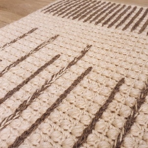 May include: A beige and brown woven rug with a textured surface. The rug has a geometric pattern of stripes and lines.