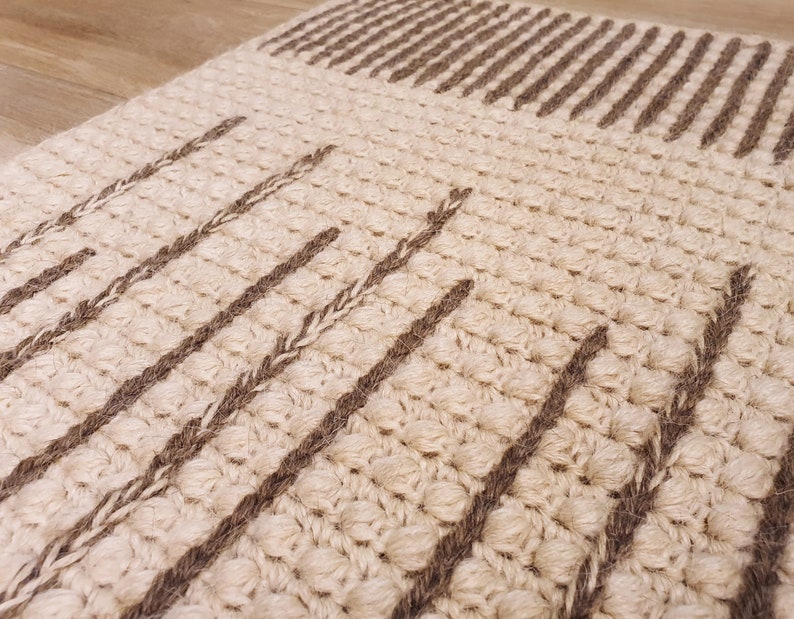 May include: A beige and brown woven rug with a textured surface. The rug has a geometric pattern of stripes and lines.
